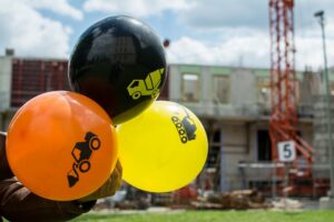 Luftballons mit Baustellensymbolen vor einer Baustelle im Hintergrund
