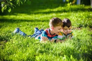 zwei Jungs liegen im Gras und schauen durch eine Lupe