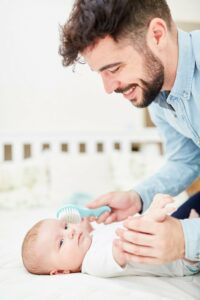 Vater entfernt mit einer Bürste Kopfschuppen bei einem neugeborenen Baby