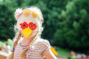 Kind mit einer Pappteller-Maske in Form eines Huhns