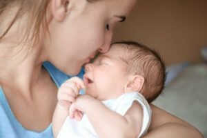 glueckliche junge frau kuesst ihr neugeborenes auf die stirn